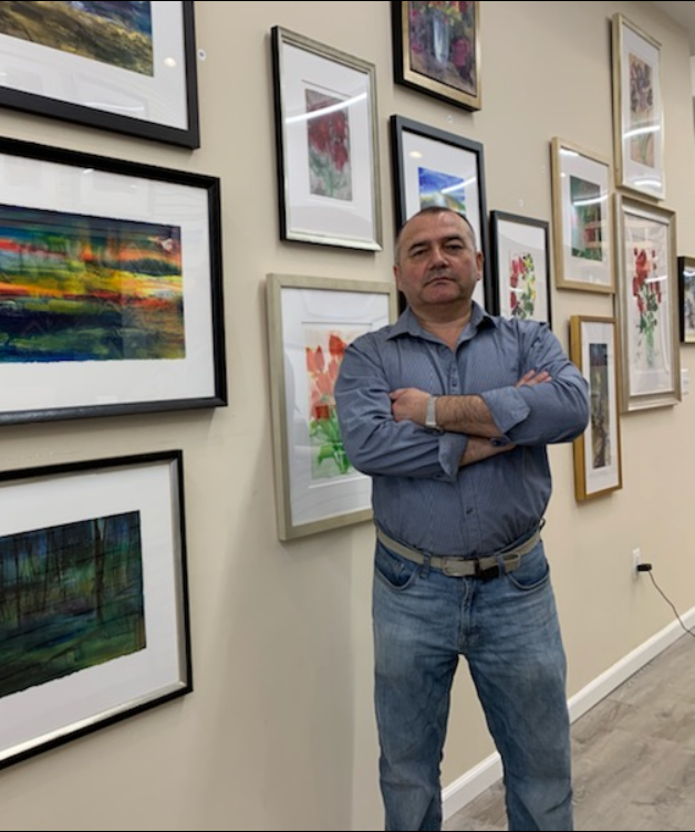 AK, owner of Experts in Framing, standing with framed artwork